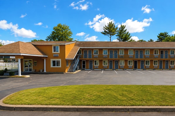 Un motel con estacionamiento y un área verde al frente.