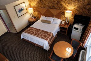 Une chambre d’hôtel comprenant un lit, des lampes de chevet, une petite table avec une chaise, un four à micro-ondes et un téléviseur.