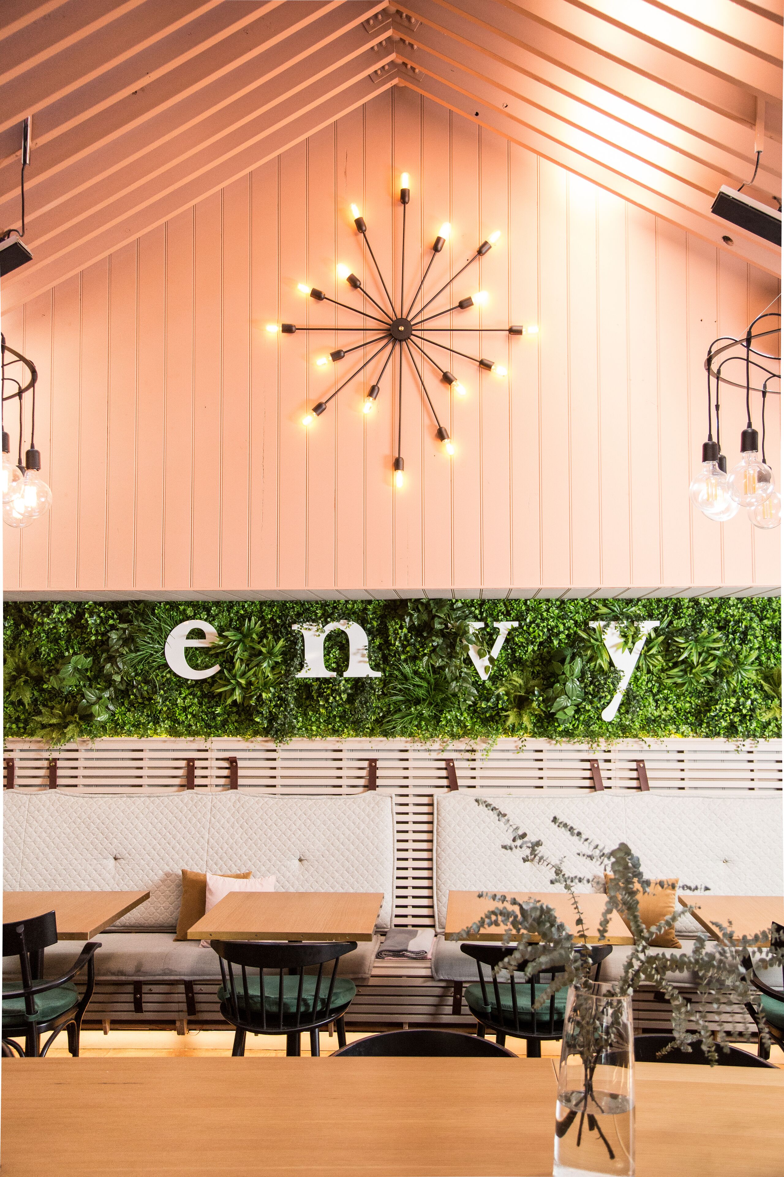 Un espace intérieur accueillant avec un plafond en bois, un luminaire fixé au mur et un mur végétal sur lequel est inscrit le mot « envie ».