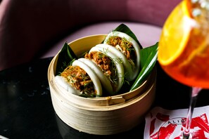 A bamboo steamer with steamed buns and a glass of orange juice on a table.