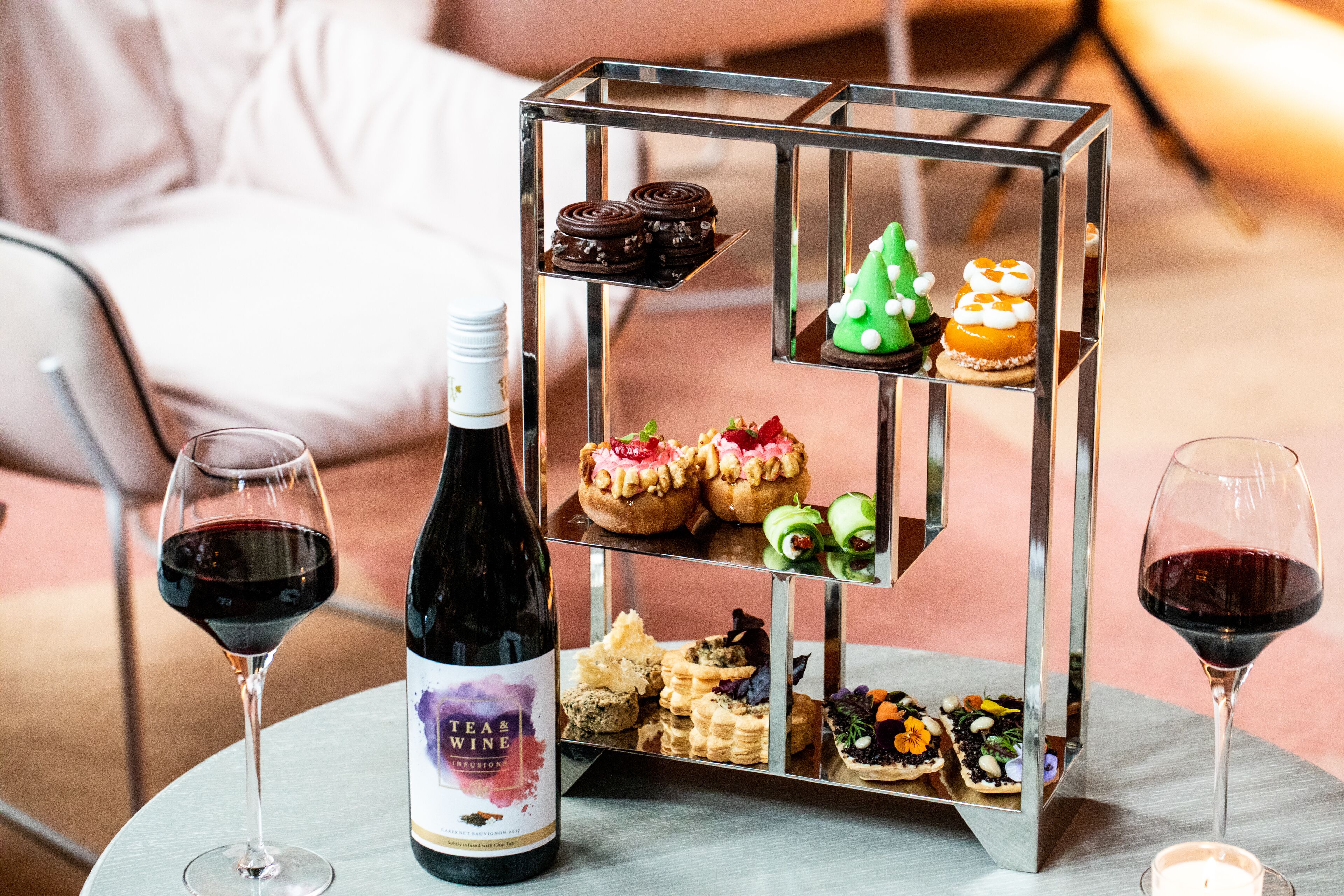 Una mesa con una botella de vino, dos copas de vino tinto y un pastel de tres niveles.