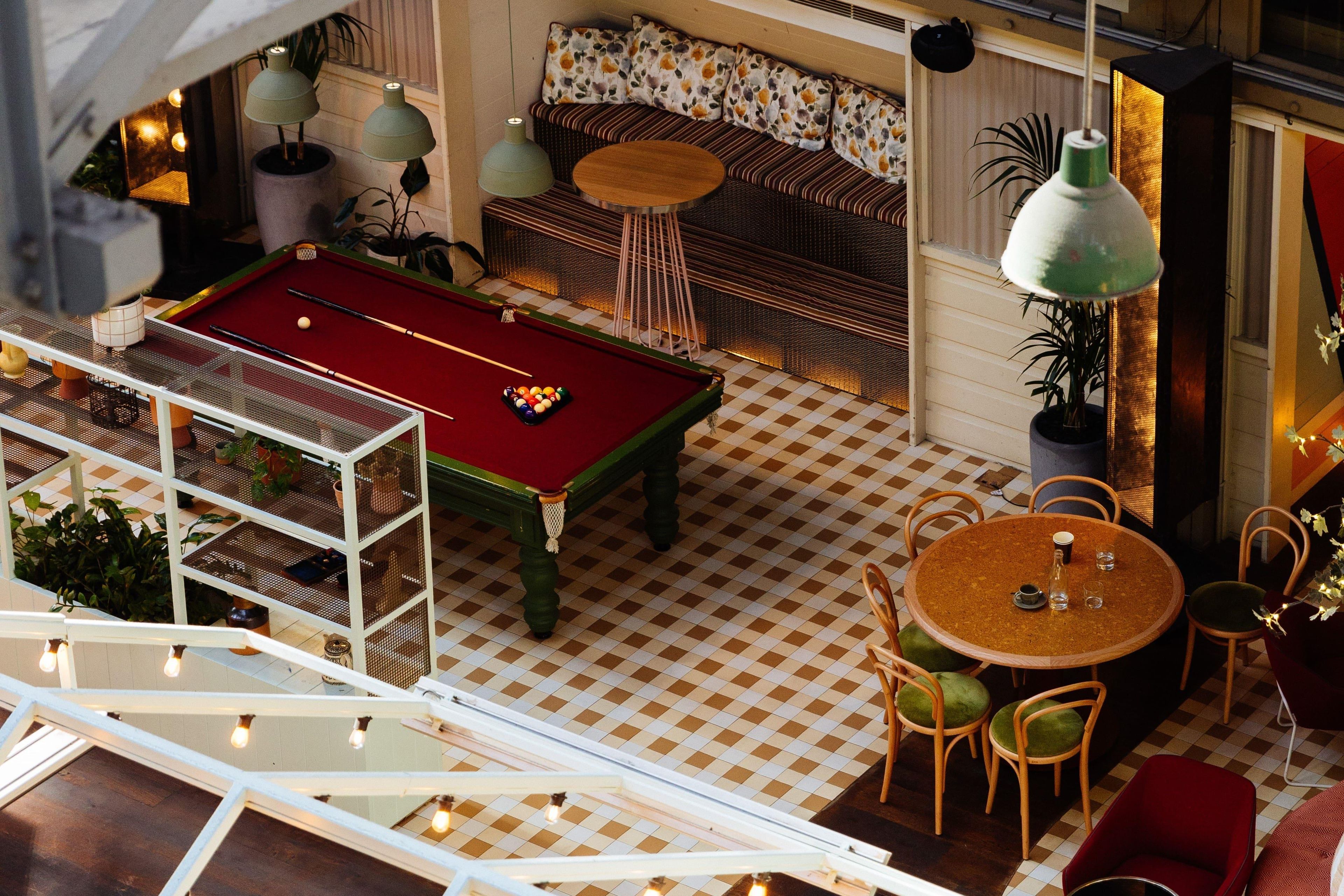 A billiards table, a sofa, a dining table with chairs, and a potted plant.