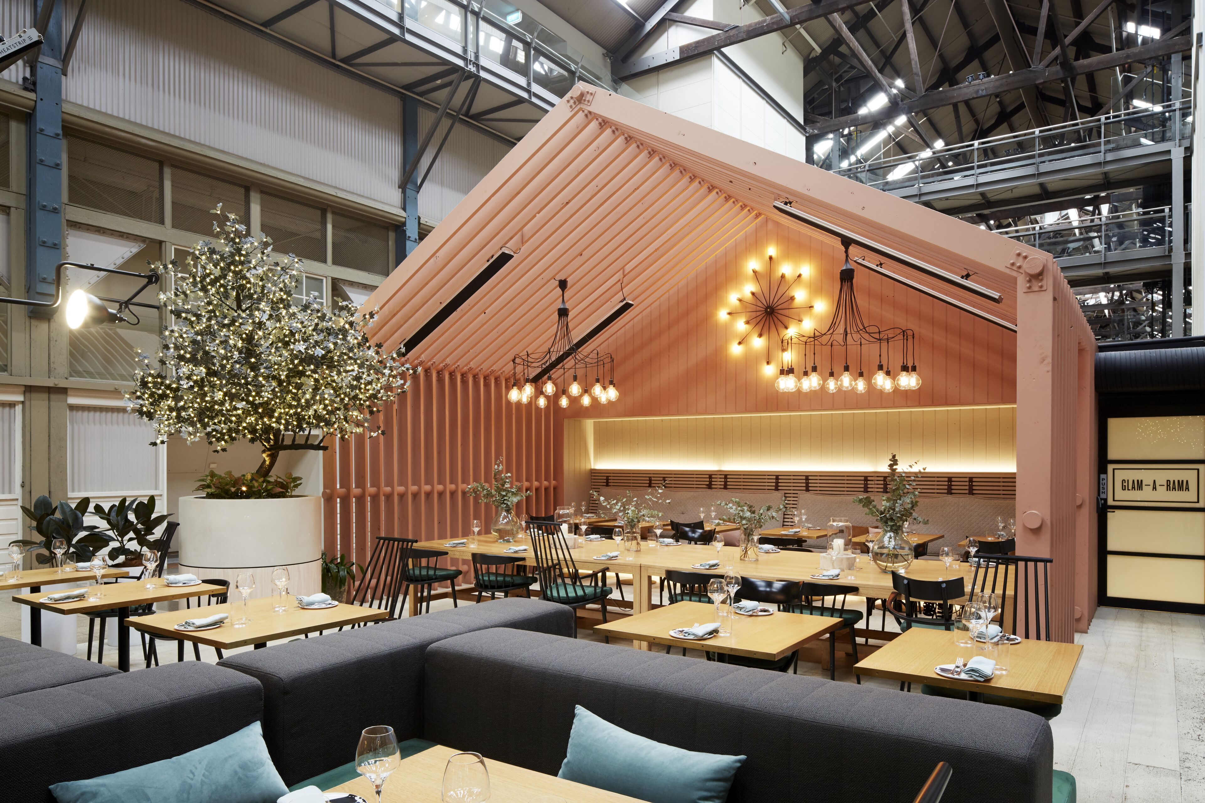 En modern restaurang med träbord, bekväma sittplatser och ett dekorativt träd.