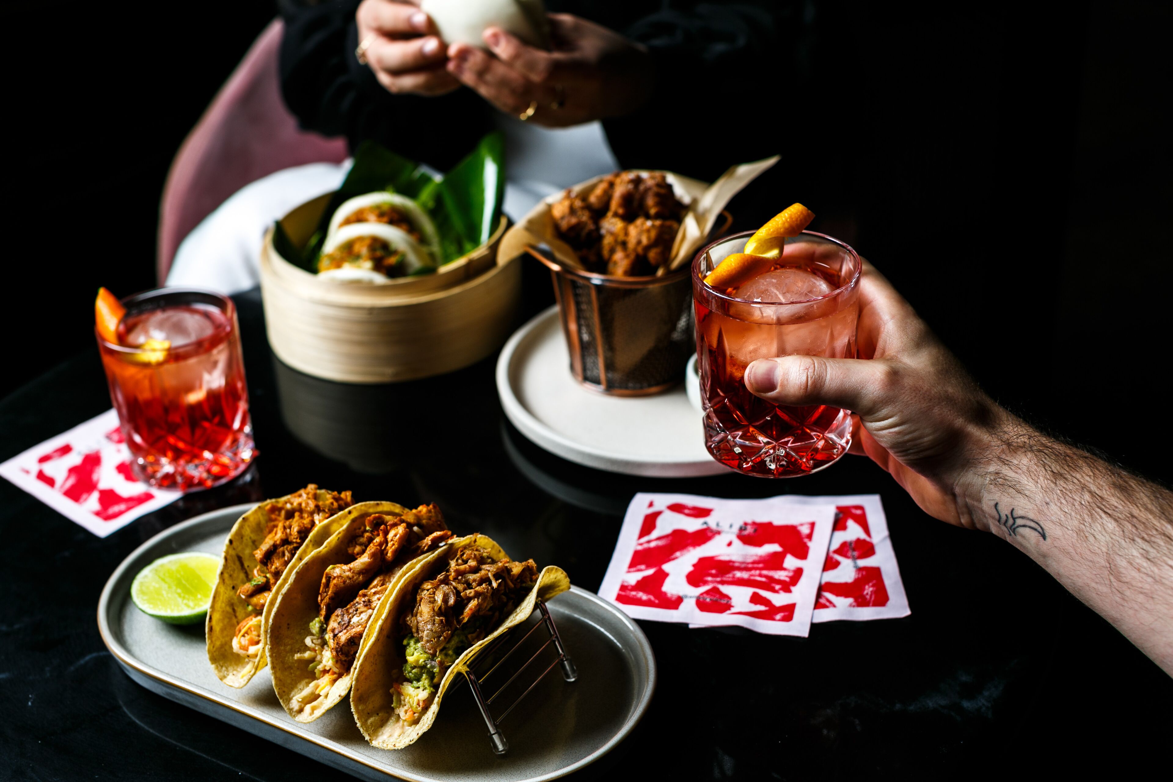 Una mesa de comedor con tacos, una bebida y cartas.