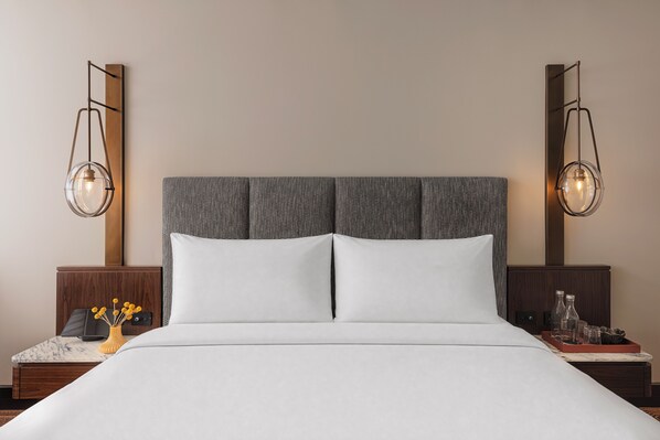 A hotel room with a large bed, two bedside tables, a nightstand, a vase with yellow flowers, and two wall-mounted lamps.