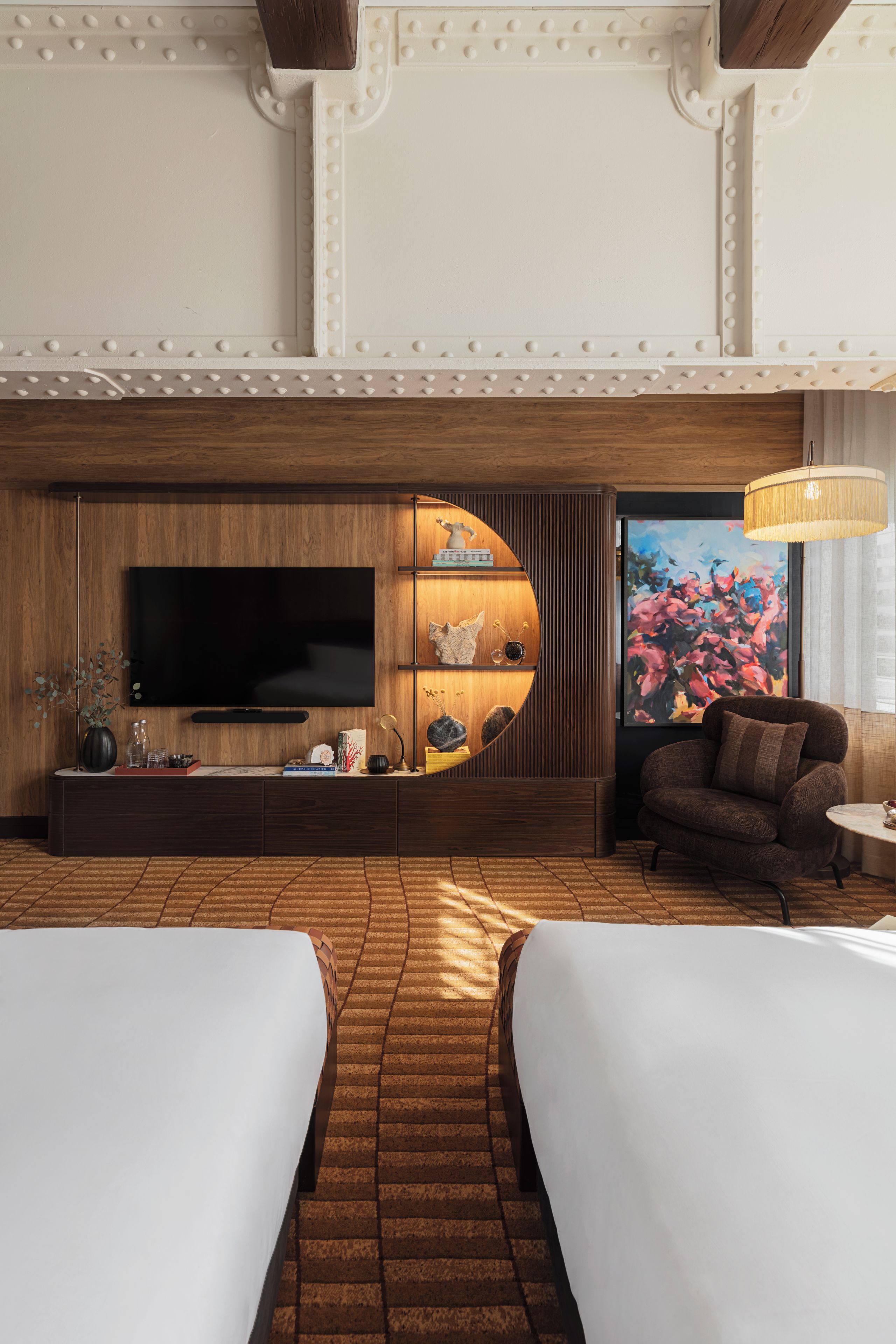 A modern hotel room with a large flat-screen TV, a wooden accent wall, a round wooden console, a sofa, and a dining table.