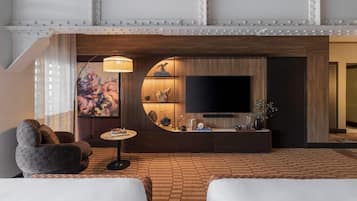 Una camera d'albergo moderna con una grande TV a schermo piatto, un tavolino rotondo in legno, un divano e un pavimento decorato.