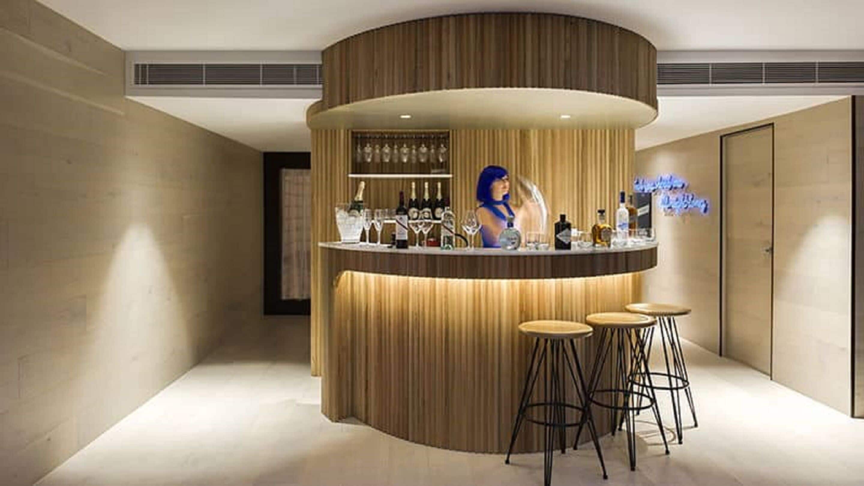 A bar area with a curved wooden counter, a bartender, and three stools.