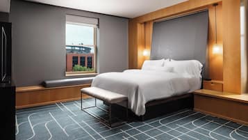 Ein modernes Hotelzimmer mit einem großen Bett, einer Sitzbank am Fenster und Blick auf die Stadtlandschaft.