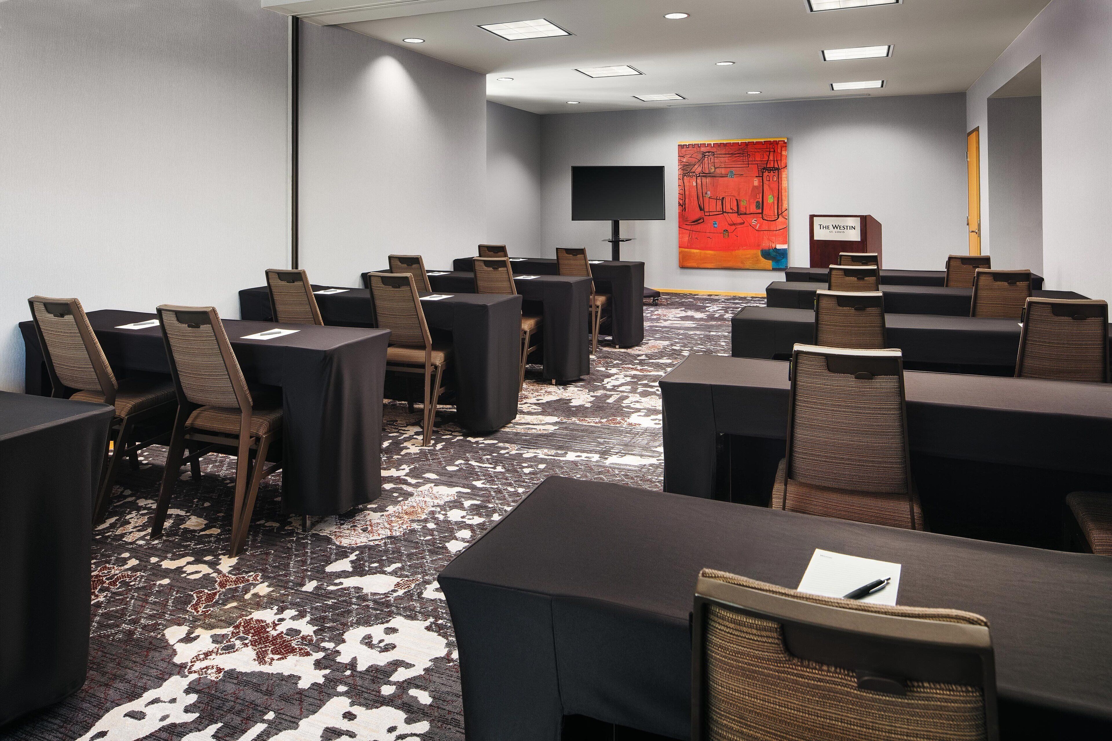 A conference room with multiple tables and chairs, a large screen, and a podium.