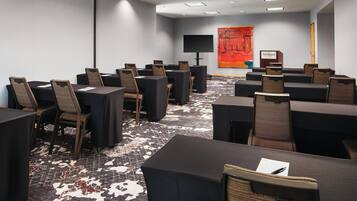 A conference room with multiple tables and chairs, a large screen, and a podium.