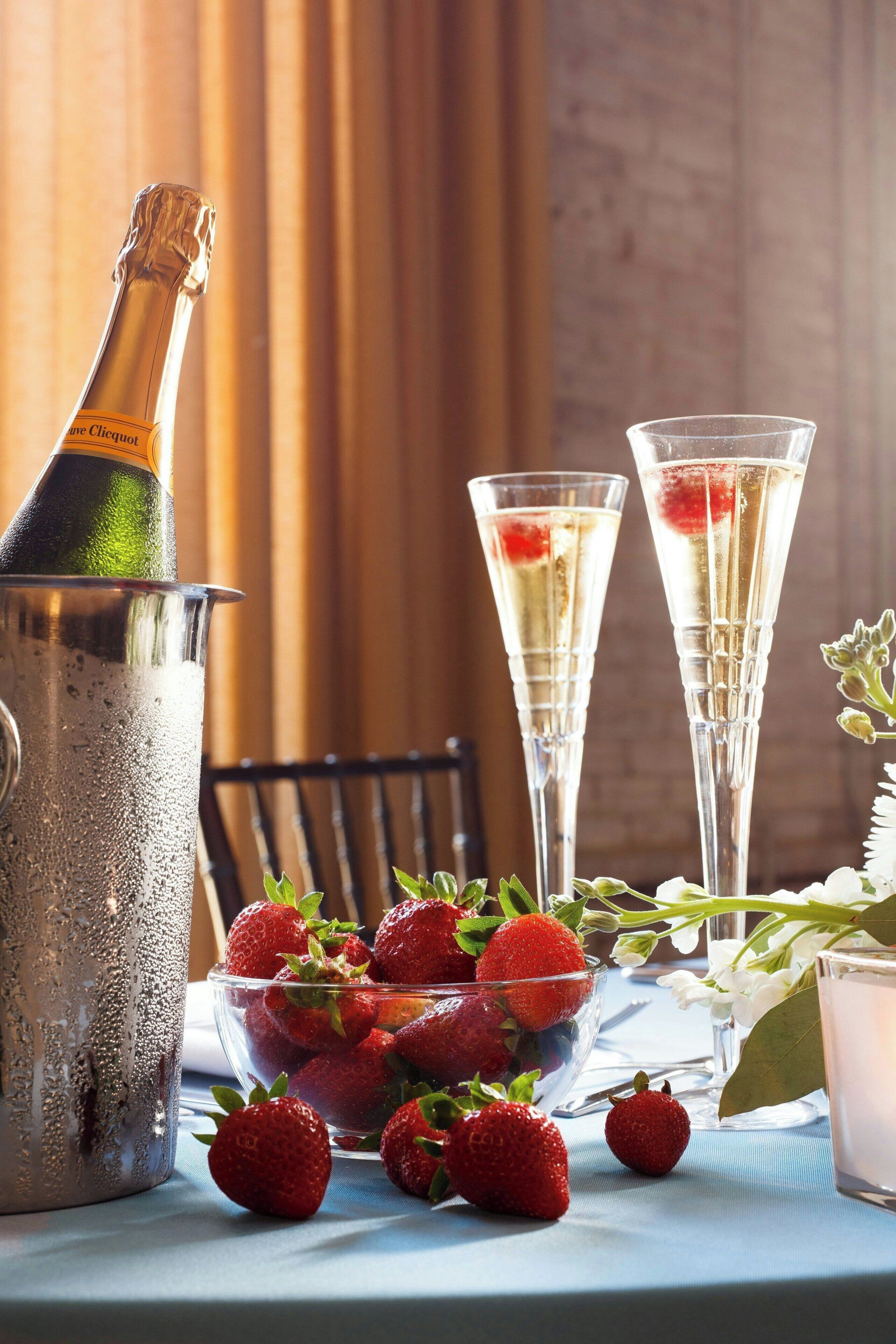 Een fles champagne, twee glazen en een schaal aardbeien op een tafel.