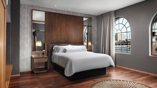 A modern hotel room with a large bed, a nightstand, a mirror, and a view of the city through arched windows. - The Westin St. Louis (St. Louis)