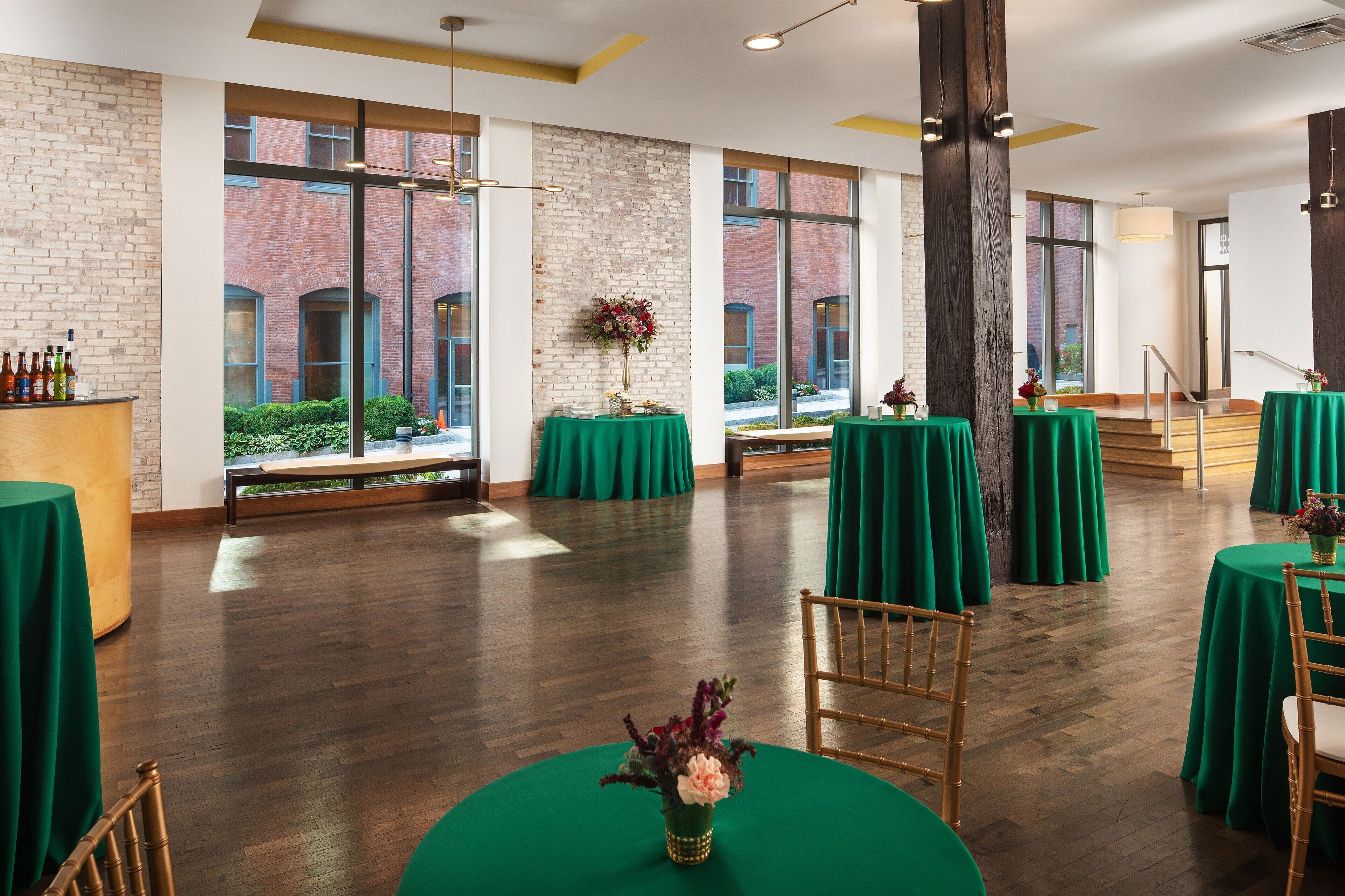 A spacious room with large windows, wooden floors, and green tablecloths.