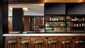 A bar area with wooden paneling, a counter, and multiple stools. - The Westin St. Louis (St. Louis)
