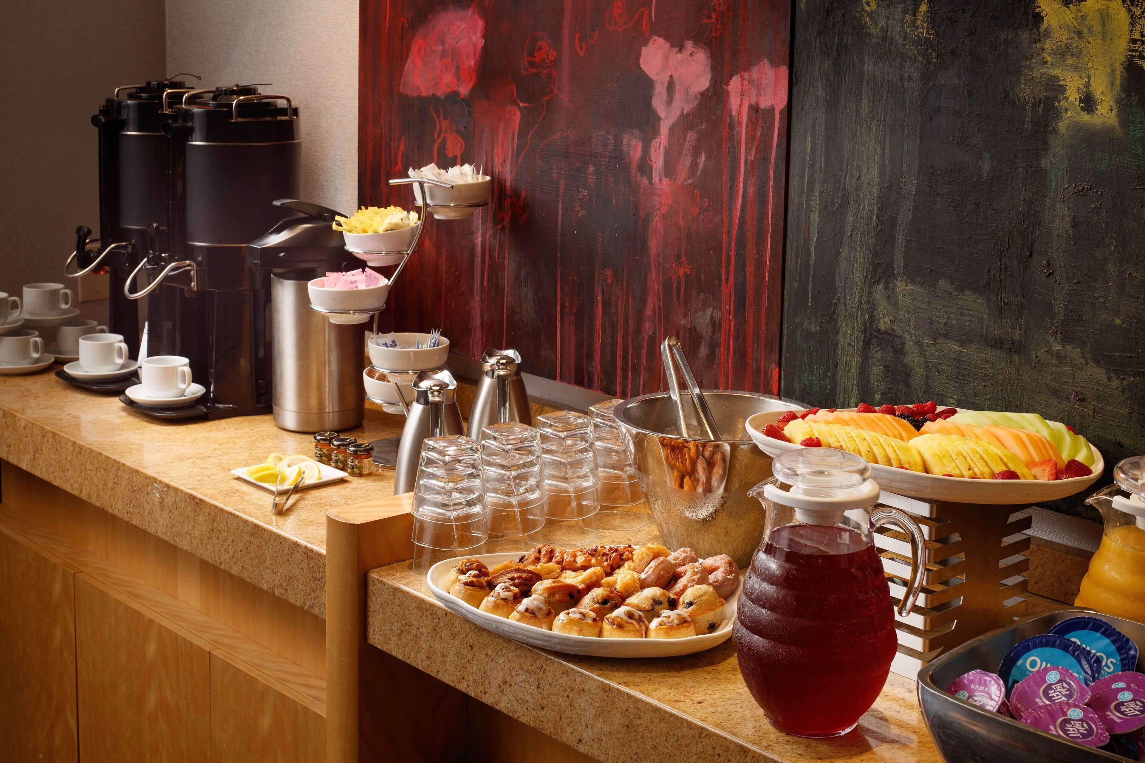 A breakfast buffet with coffee makers, fruit, pastries, and beverages.