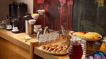 A breakfast buffet with coffee makers, fruit, pastries, and beverages.