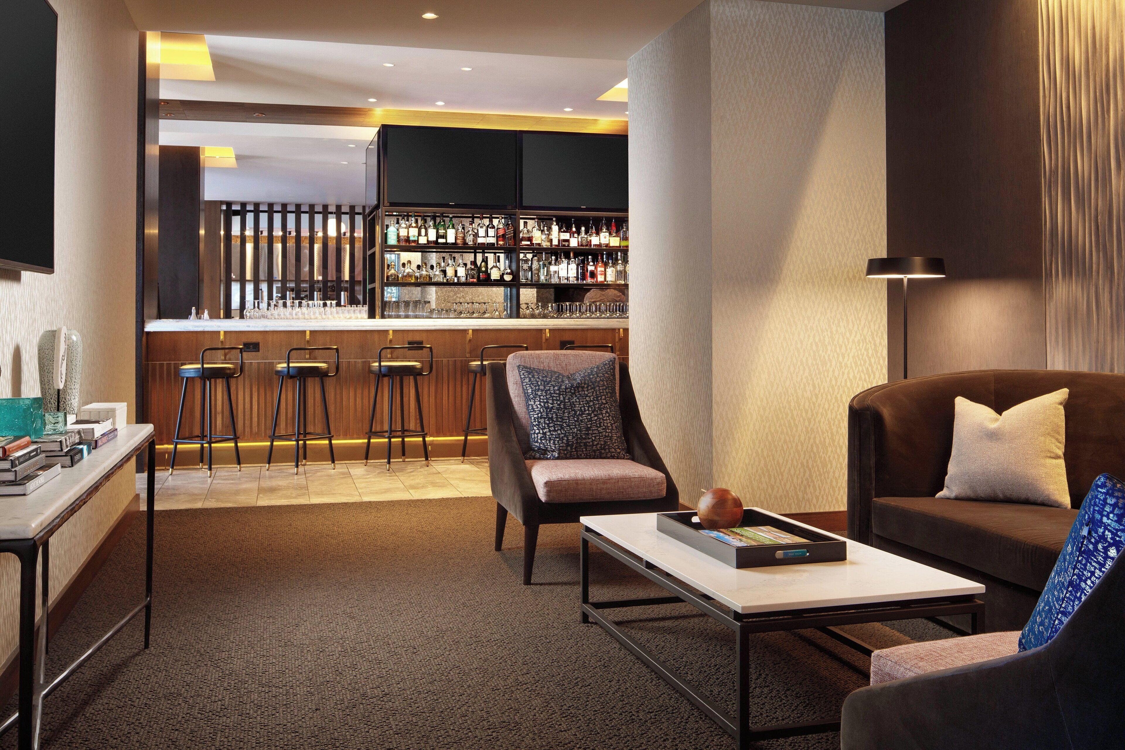 A modern hotel lobby with a bar area, seating, and a reception desk.