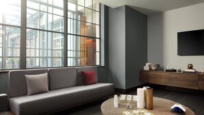 A modern living room with a grey sofa, a round wooden coffee table, and a large window with a city view. - The Westin St. Louis (St. Louis)
