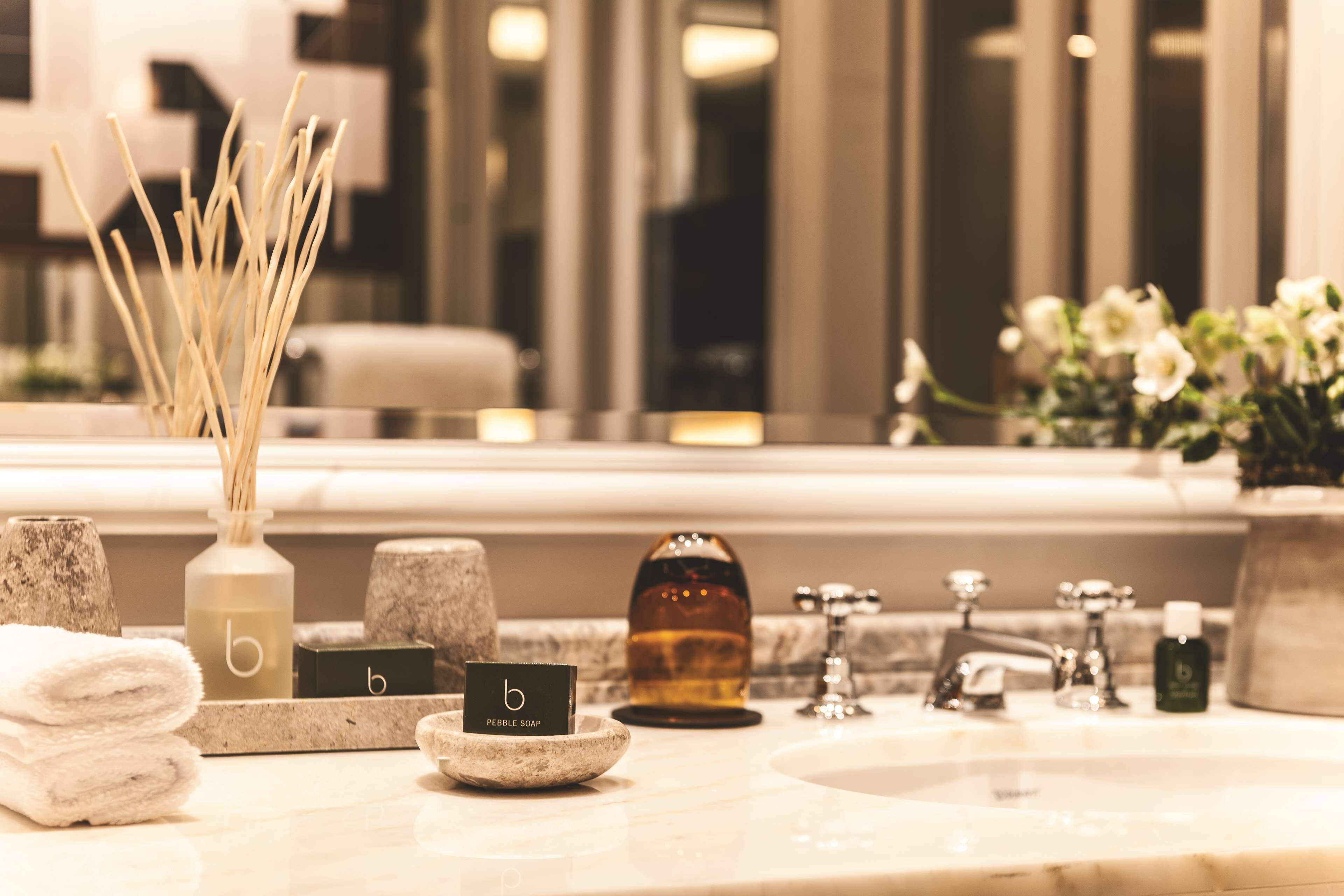 A bathroom with a marble sink, a bottle of soap, a towel, and a decorative vase with reeds.
