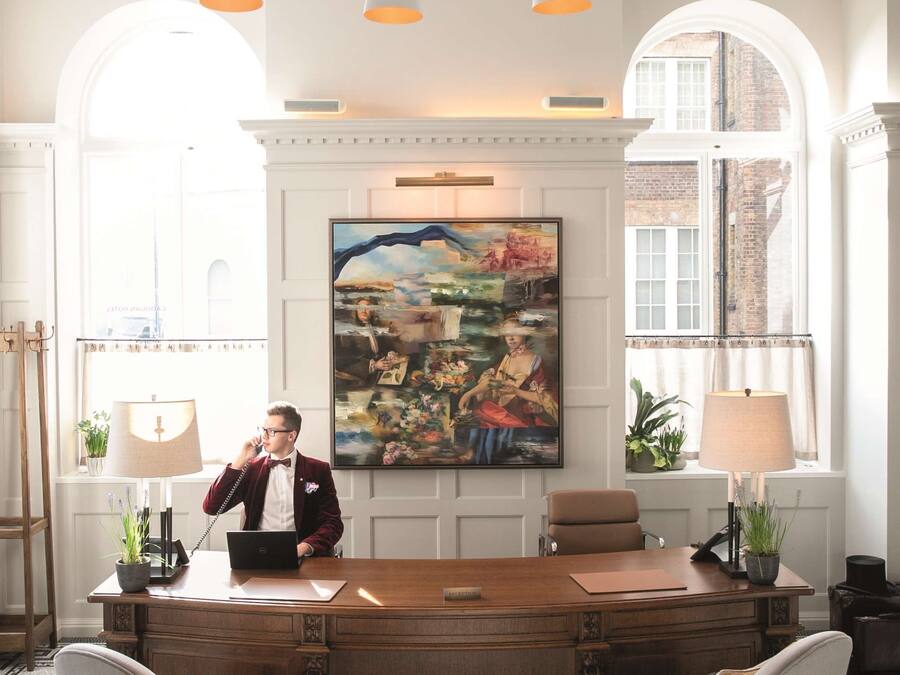 A well-lit office with a wooden desk, two chairs, and a large painting on the wall.