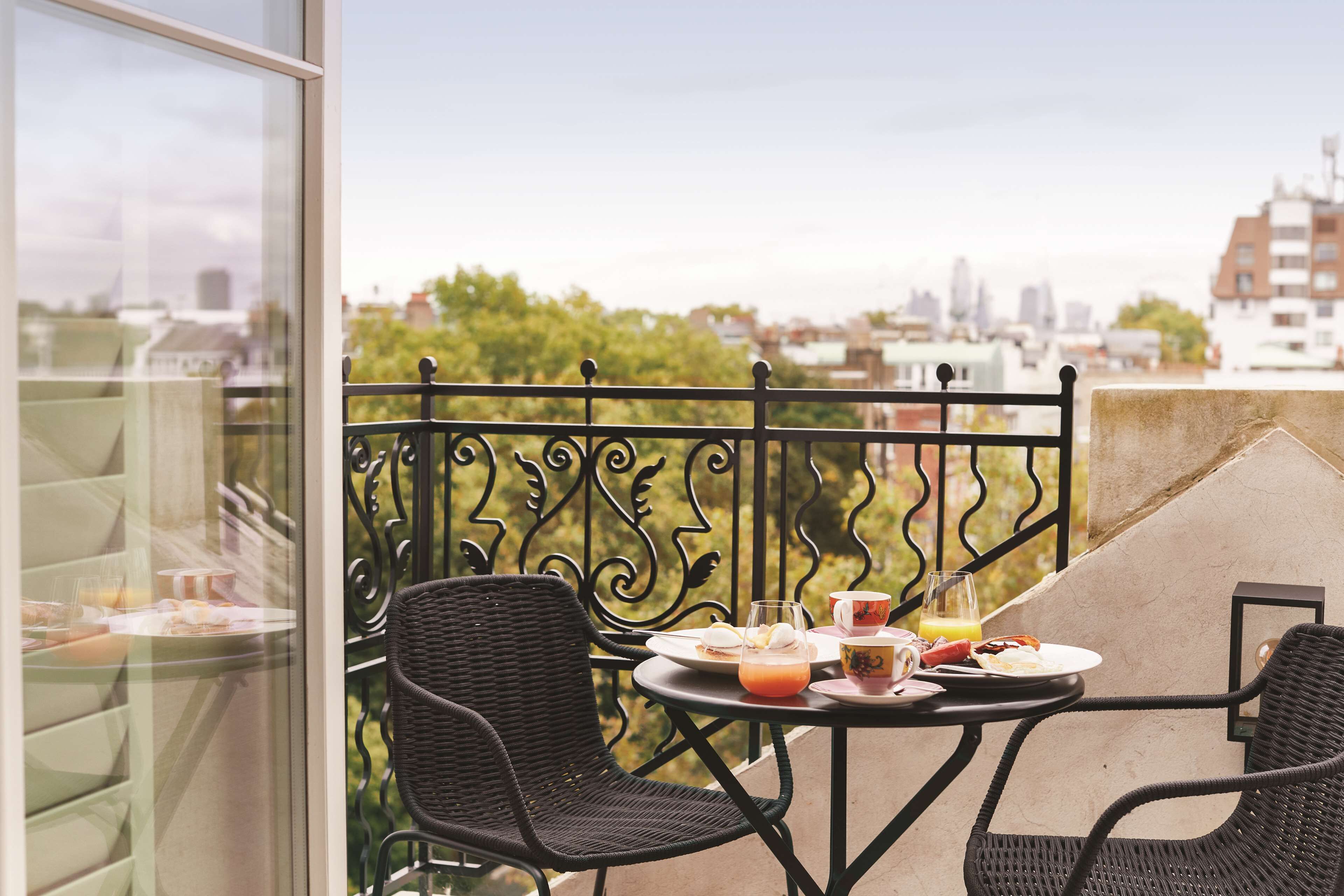 A balcony with wicker chairs, a table with breakfast items, and a city view.