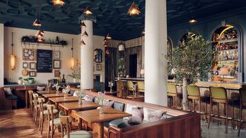 A restaurant interior with wooden tables, chairs, hanging pendant lights, a bar area, and a menu board.