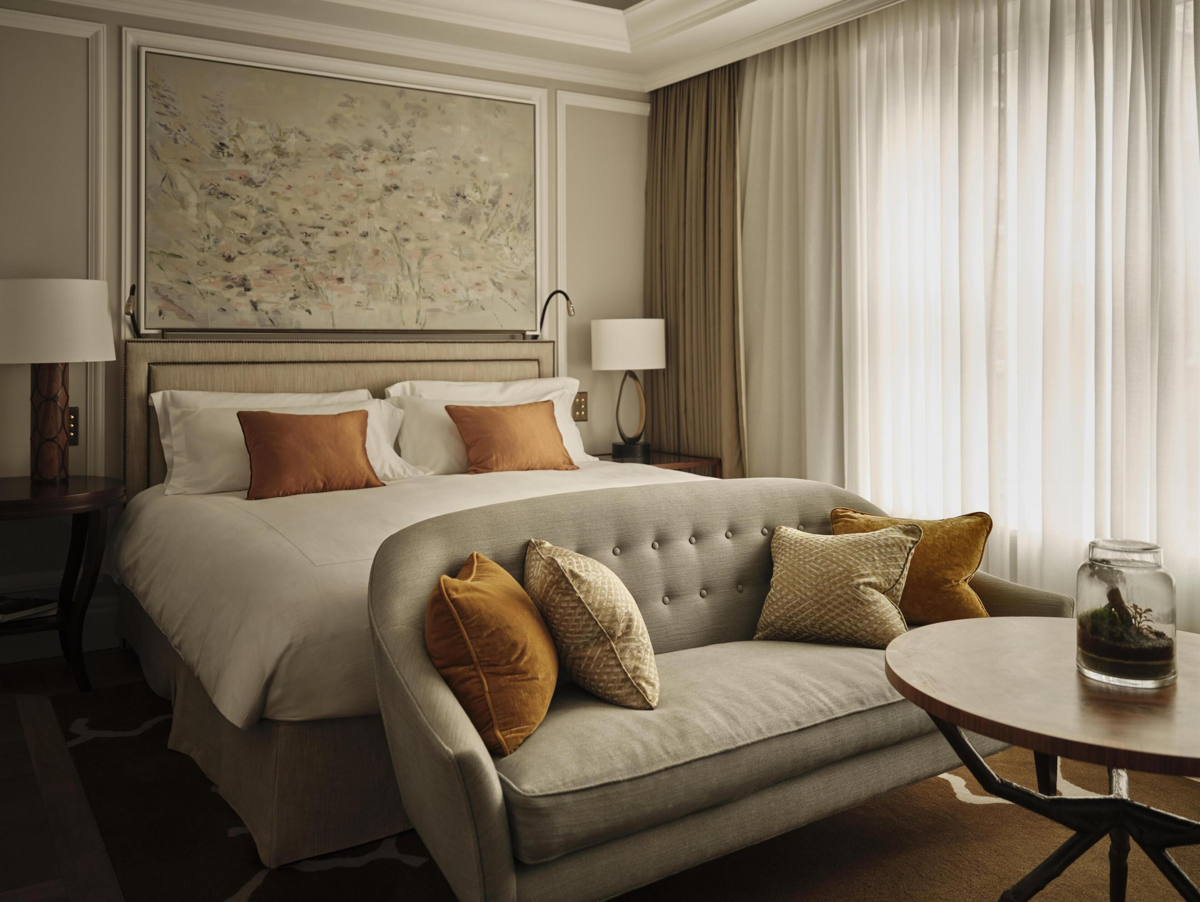 A hotel room with a large bed, a sofa, a round table, and a large abstract painting on the wall.