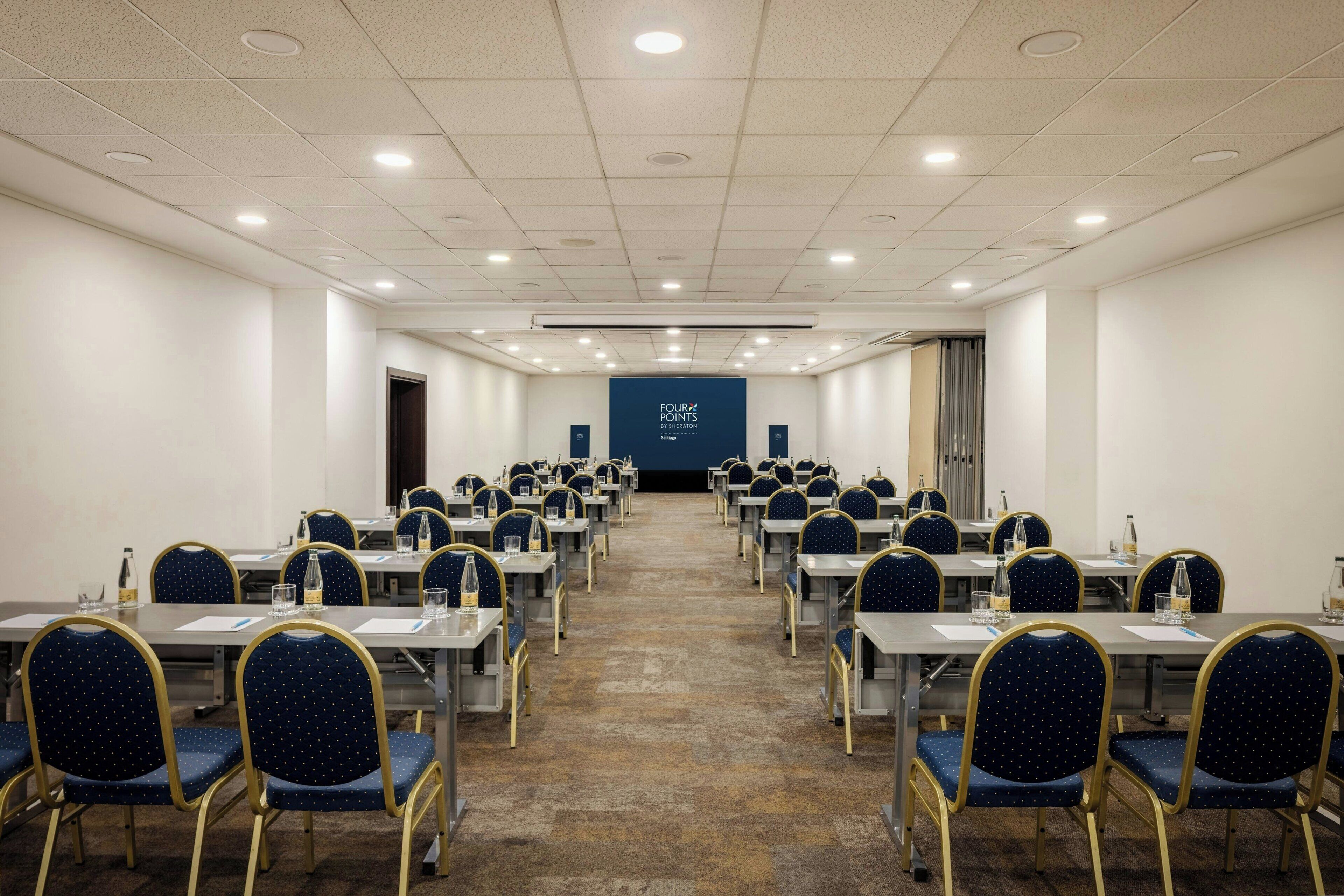 Ein Konferenzraum mit Reihen von Tischen und Stühlen, einer Projektionsleinwand und einem Teppichboden.
