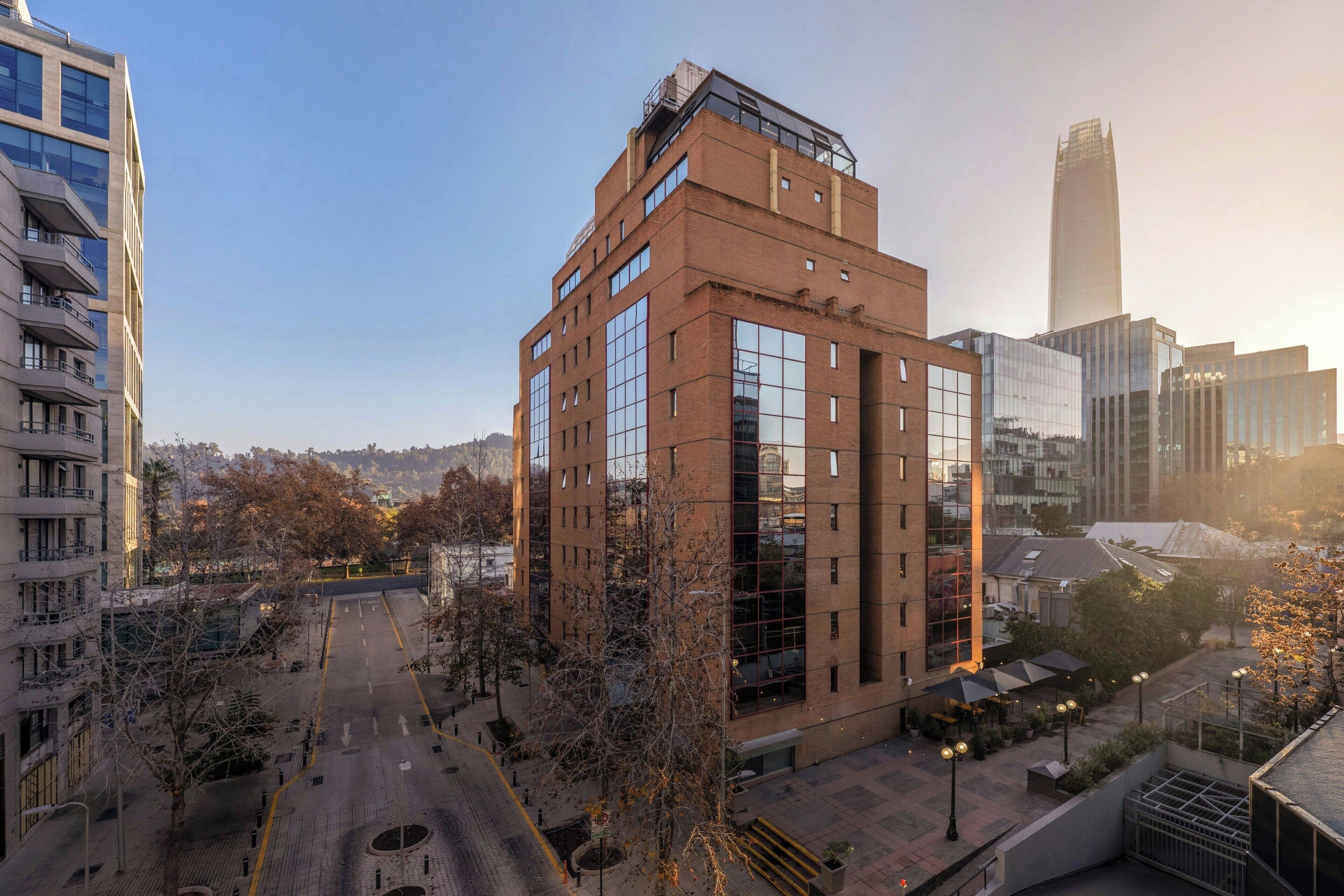 A modern building with a glass facade, surrounded by other high-rise buildings and a clear sky.
