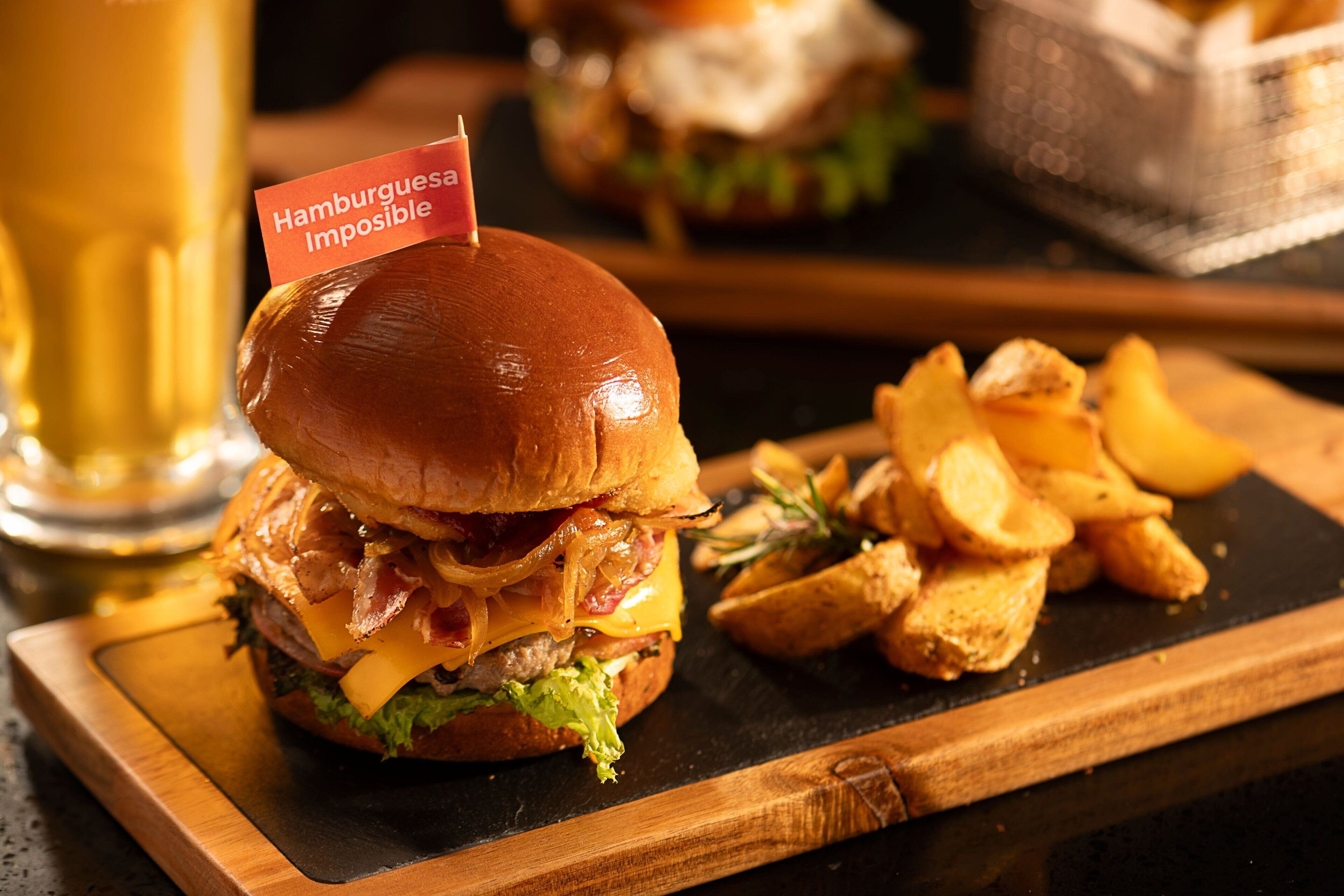 Un hamburger avec une étiquette indiquant « Hamburguesa Imposible », servi avec des frites sur une planche en bois.