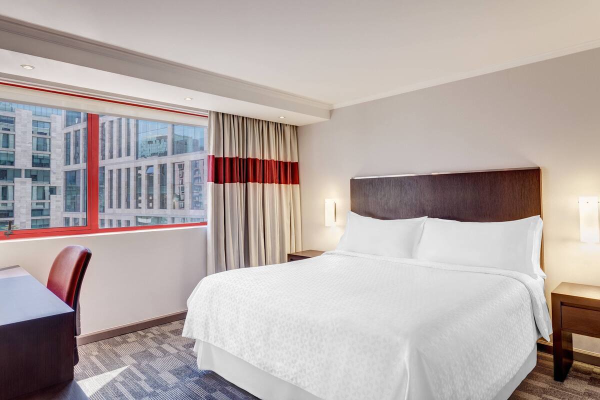 Een hotelkamer met een groot bed, een bureau en uitzicht op een stadsbeeld door het raam.