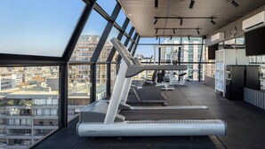 A gym with treadmills and exercise equipment, large windows with a city view, and a modern ceiling design.
