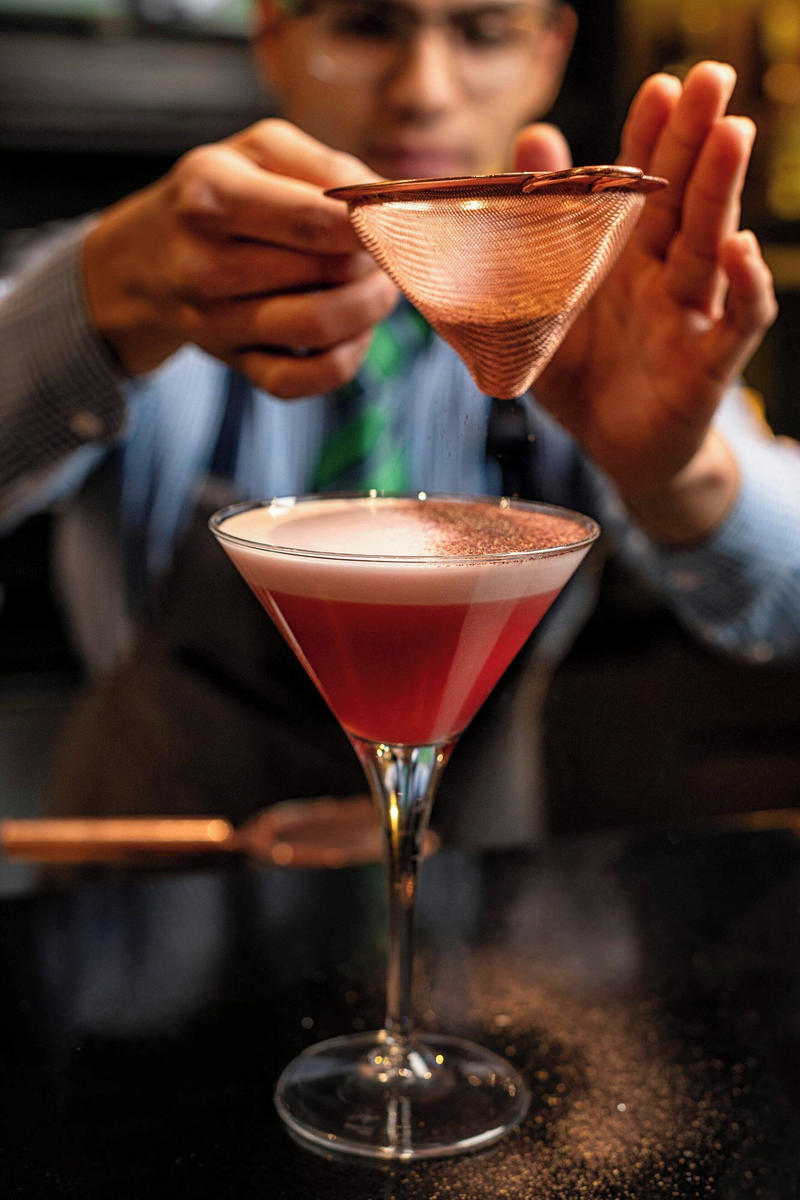 A bartender preparing a cocktail with a copper strainer.