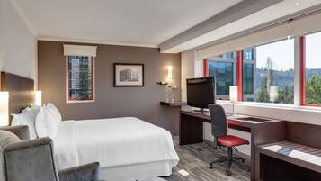 Habitación de hotel con una cama grande, un escritorio con computadora, una silla y vista al exterior.