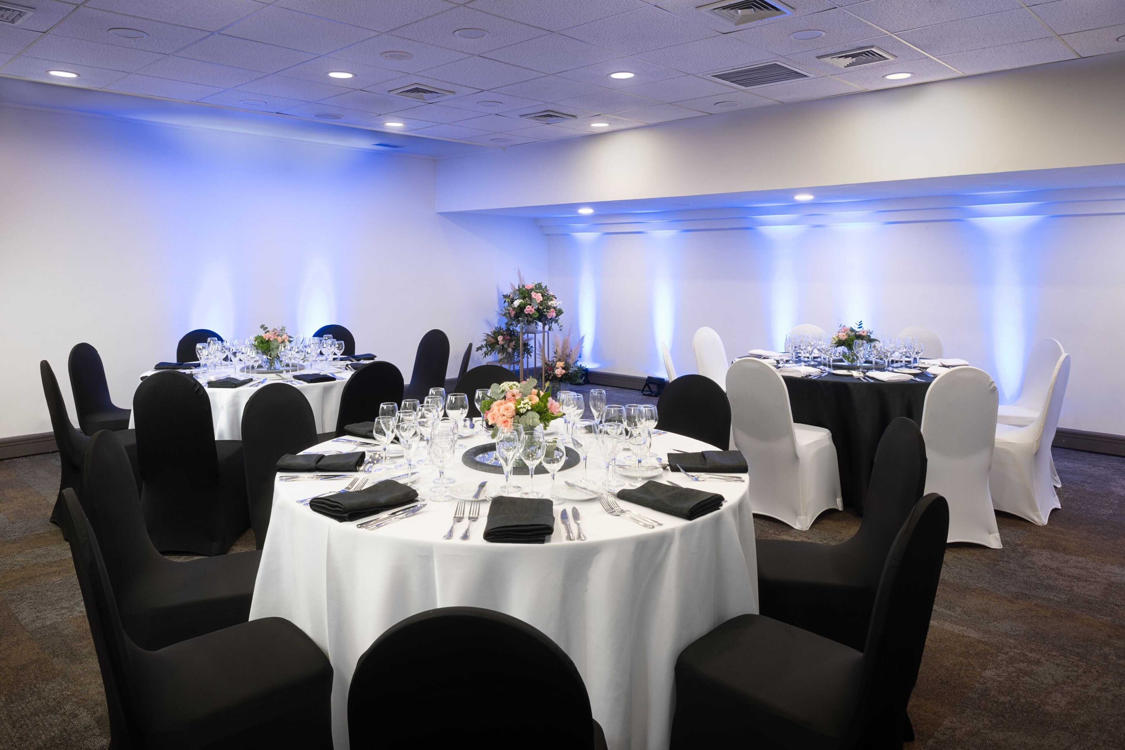 A conference room with round tables, black chairs, white tablecloths, and floral centerpieces.