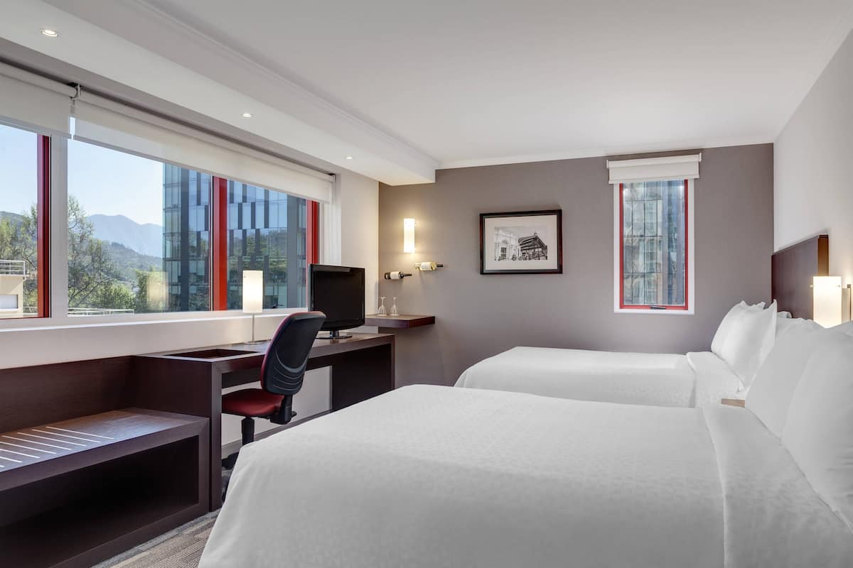 Hotelkamer met twee bedden, een bureau met een computer, een stoel en een raam met uitzicht op bergen.