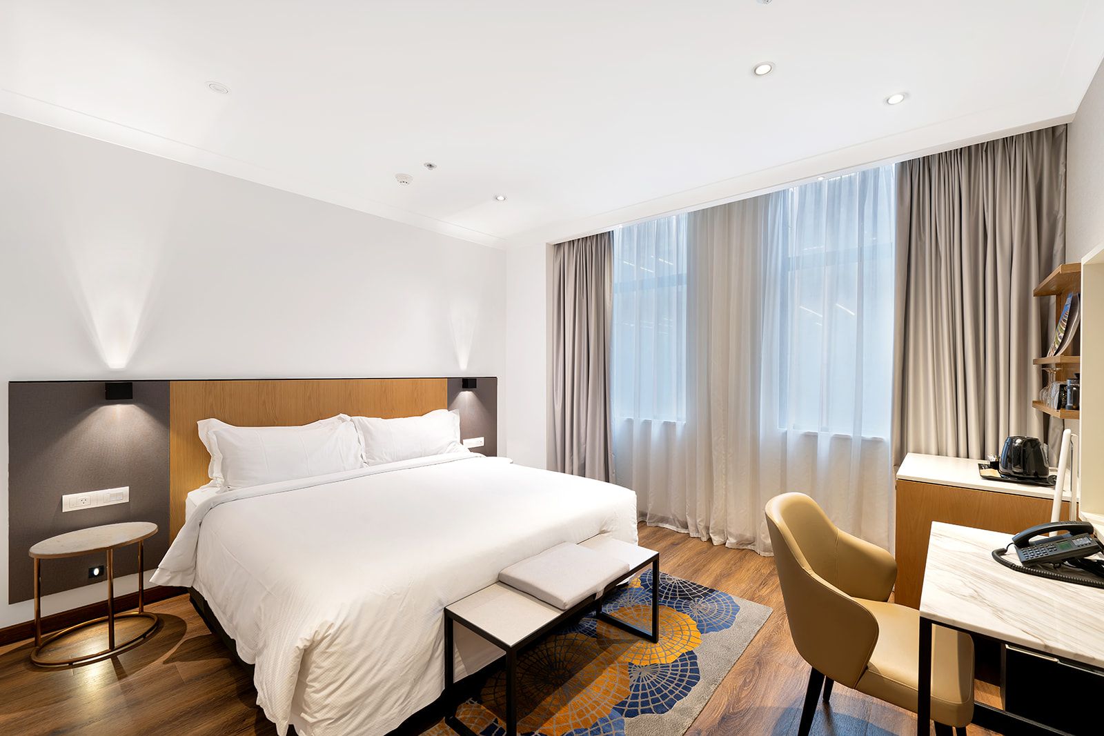 Ein Hotelzimmer mit Bett, Nachttisch, Stuhl, Schreibtisch und einem großen Fenster mit Vorhängen.