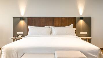 Une chambre d’hôtel moderne avec un grand lit, deux tables de chevet avec des lampes et une tête de lit en bois.