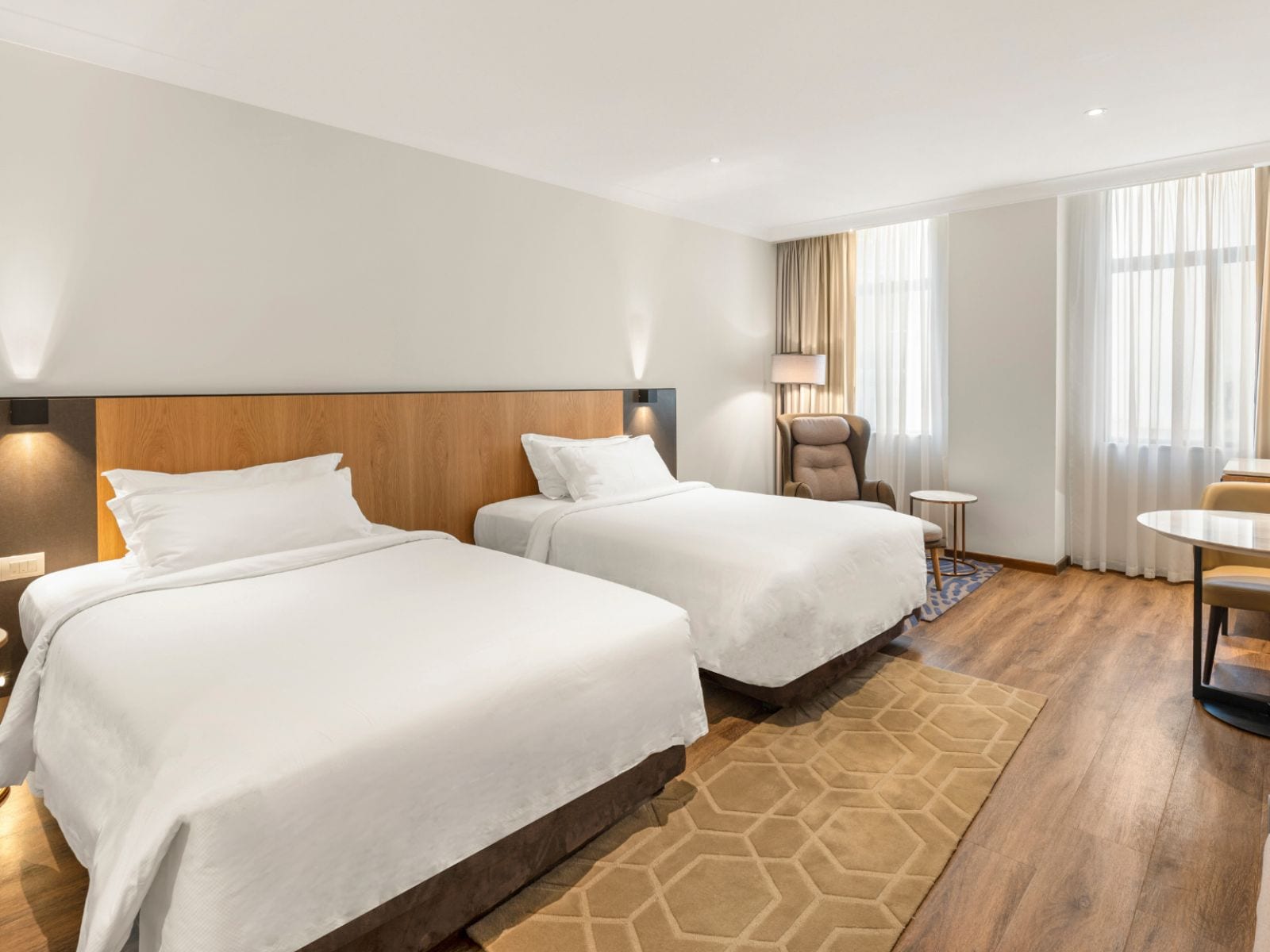 Habitación de hotel con dos camas, una silla, una mesita y una ventana con cortinas.