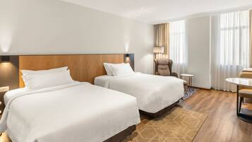 Habitación de hotel con dos camas, una silla, una mesita y una ventana con cortinas.