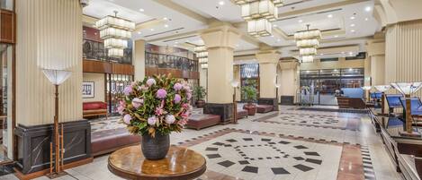 A spacious lobby with a central round table, multiple seating areas, and a decorative floor pattern.