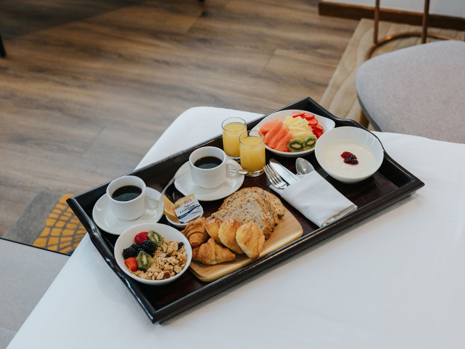 Una bandeja de desayuno con croissants, fruta, yogur, café y jugo.