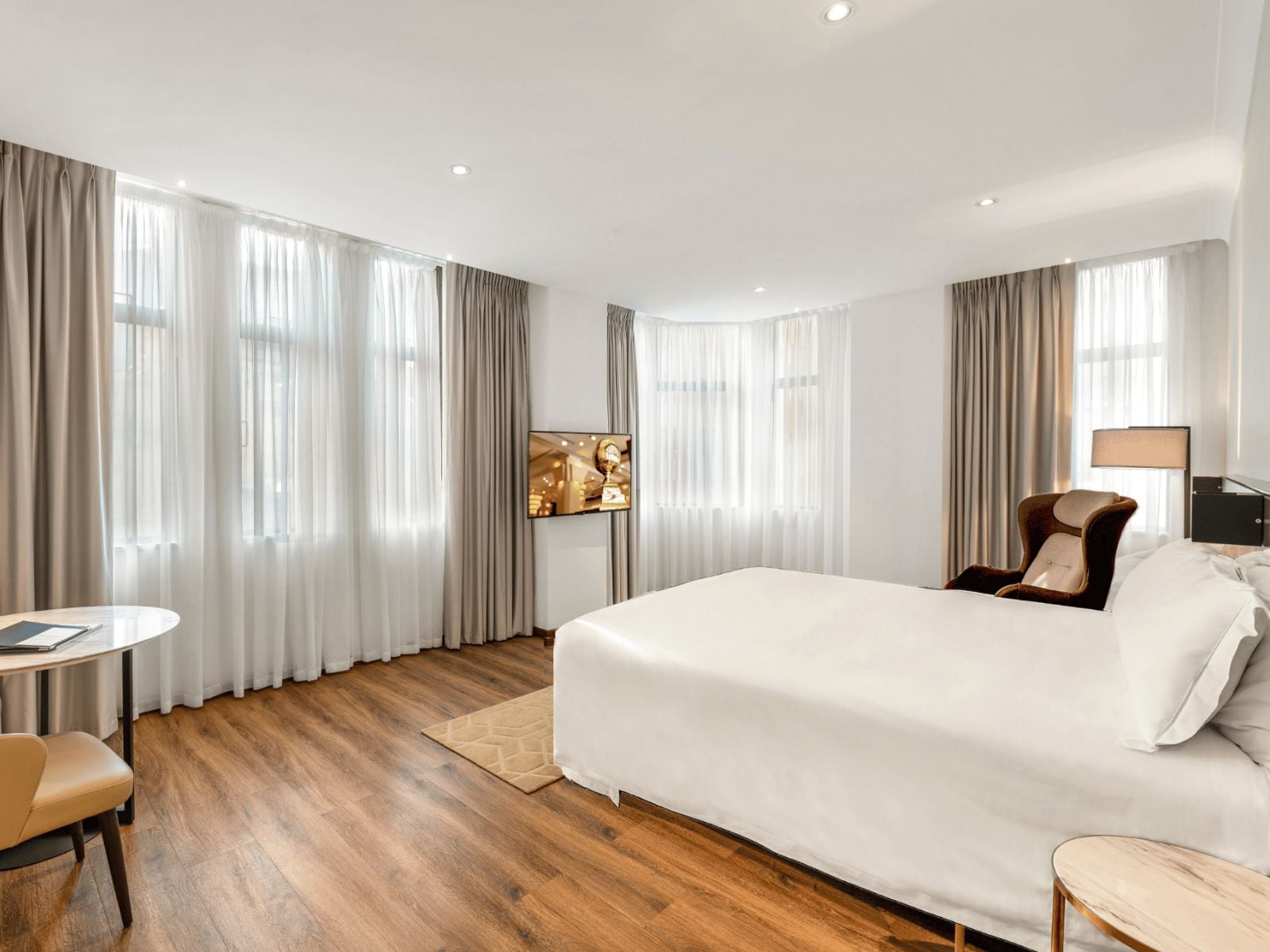 A hotel room with a large bed, a desk, a chair, and a television mounted on the wall.