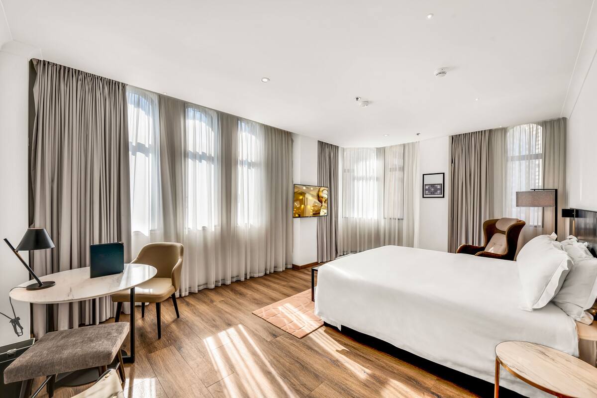 A modern hotel room with a large bed, a desk with a chair, a small table, and a sofa.
