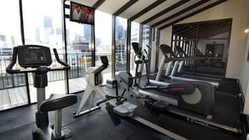 Un gimnasio moderno con diversos equipos de ejercicio, amplias ventanas y vistas a la ciudad.