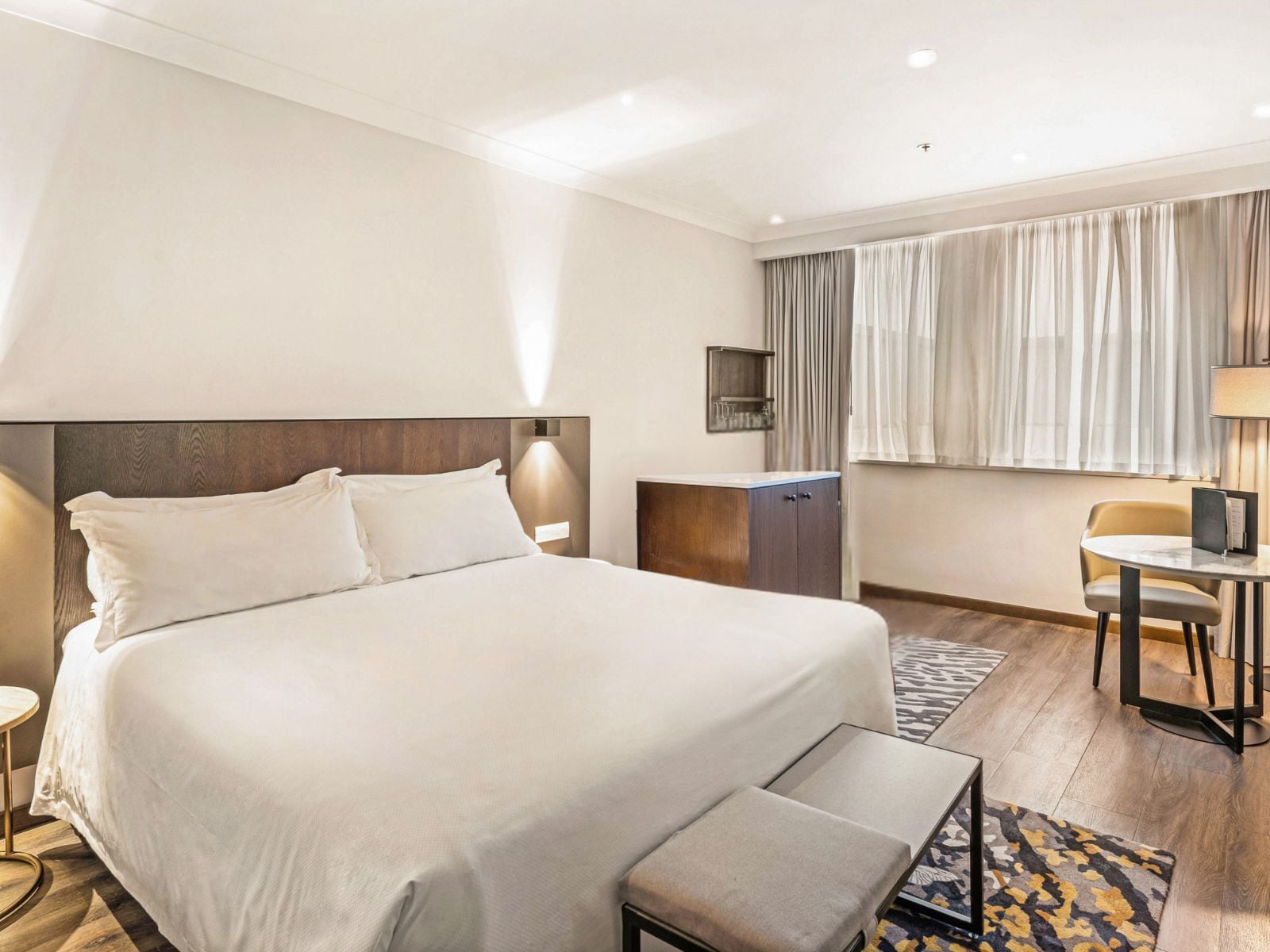 A hotel room with a large bed, a desk, a chair, and a small table.