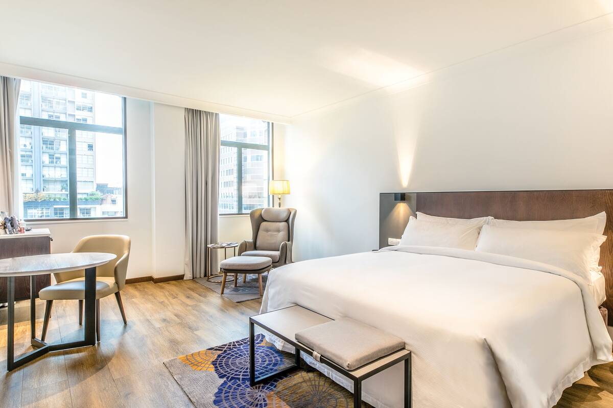A hotel room with a bed, a desk, a chair, and a view of the city.