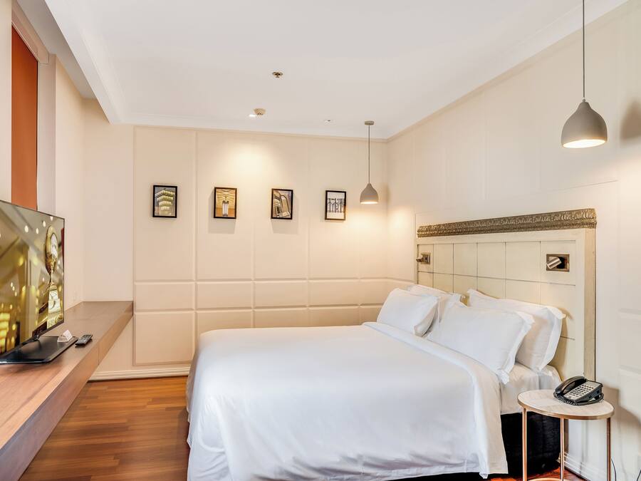 A modern hotel room with a large bed, a bedside table with a phone, a TV, and framed artwork on the wall.