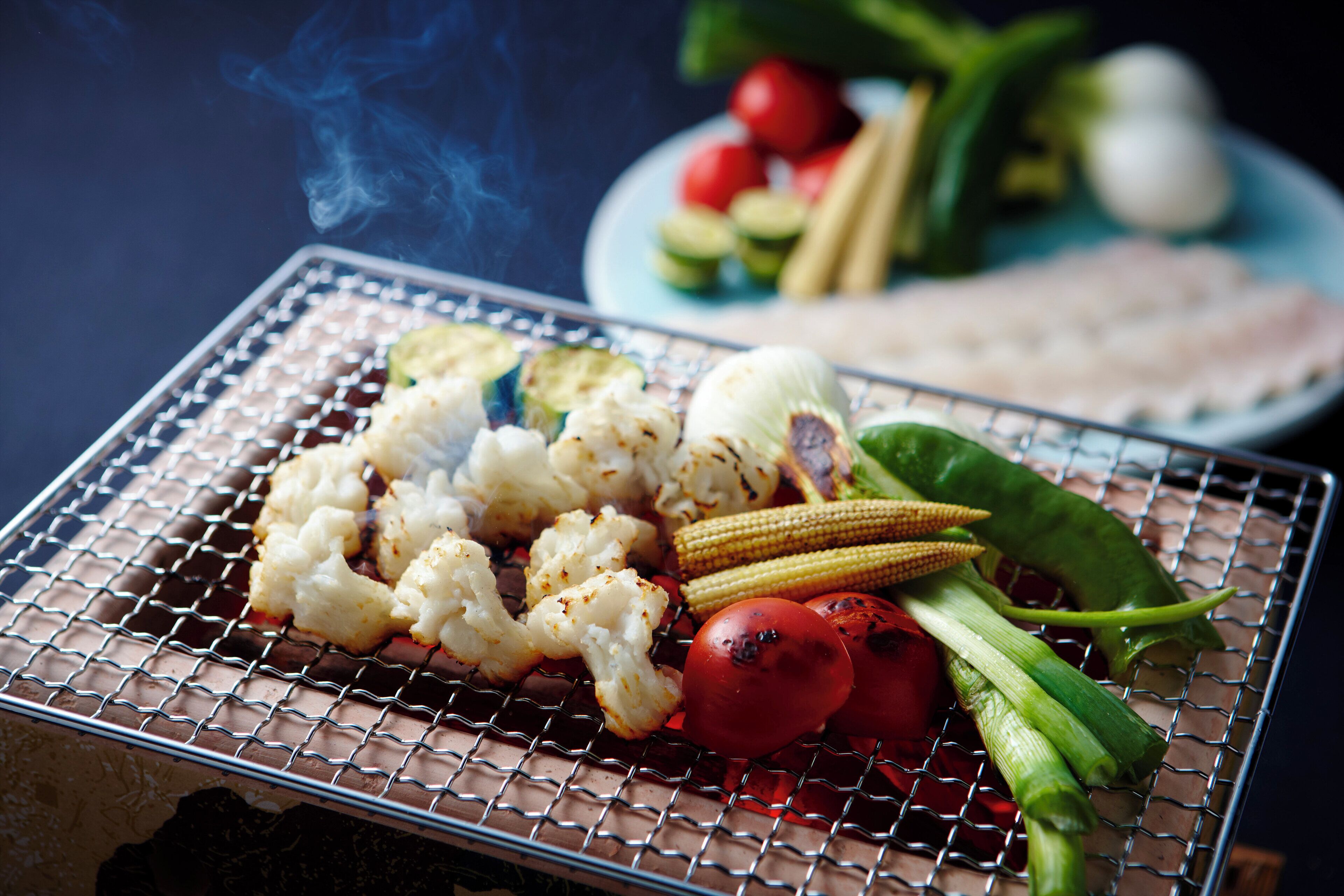 A grill with vegetables and meat, with smoke rising.